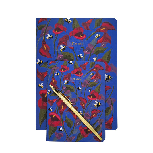 Two soft cover notebooks with floral design and a gold pen on a white background